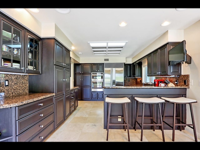 kitchen featuring dark brown cabinetry, tasteful backsplash, stainless steel appliances, and dark stone counters