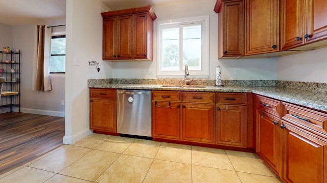 kitchen with brown cabinets, light stone counters, a sink, baseboards, and stainless steel dishwasher