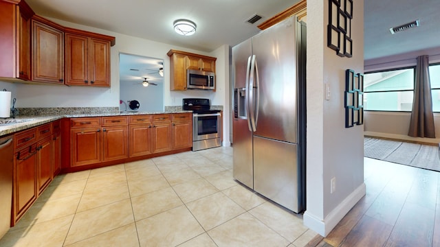 kitchen with appliances with stainless steel finishes, light stone counters, light tile patterned floors, and ceiling fan