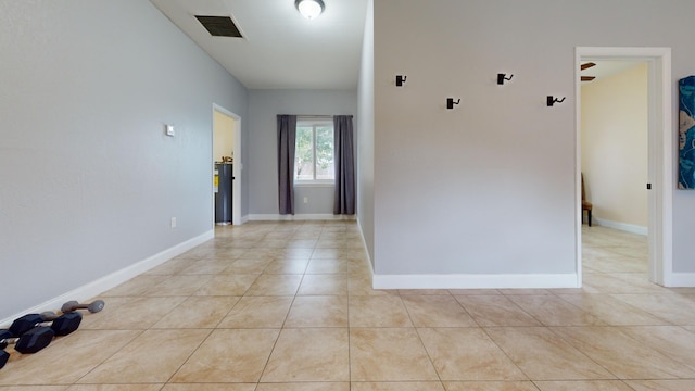 unfurnished room featuring water heater, baseboards, light tile patterned flooring, and visible vents