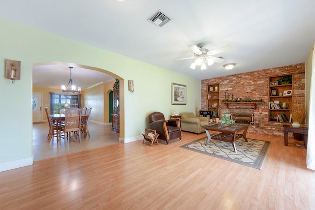 living room with light wood-type flooring, ceiling fan with notable chandelier, built in features, and a fireplace