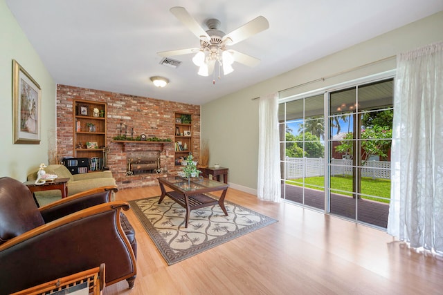 living room with ceiling fan, built in features, a fireplace, and light hardwood / wood-style flooring