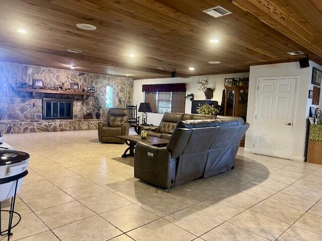 living room featuring a stone fireplace, wooden ceiling, and light tile patterned floors