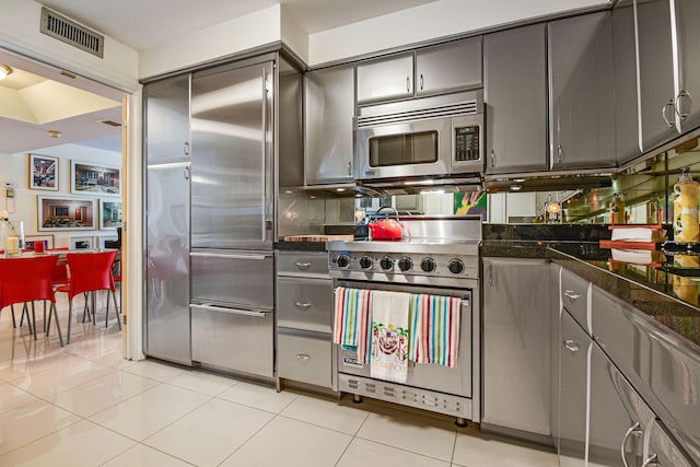 kitchen featuring appliances with stainless steel finishes, light tile patterned flooring, and dark stone countertops