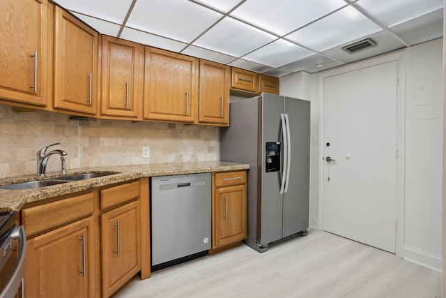 kitchen featuring sink, backsplash, stainless steel appliances, light stone countertops, and light wood-type flooring