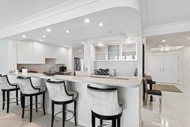 kitchen featuring stainless steel fridge, a kitchen bar, light tile floors, white cabinets, and tasteful backsplash