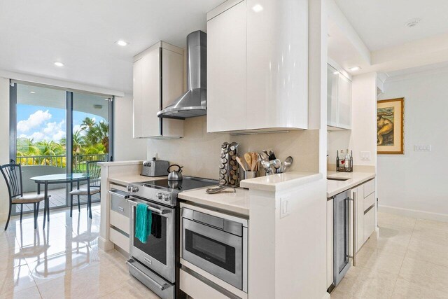 kitchen featuring light tile flooring, appliances with stainless steel finishes, white cabinets, beverage cooler, and wall chimney range hood