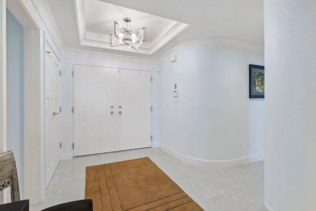 tiled entrance foyer with a chandelier, a raised ceiling, and ornamental molding