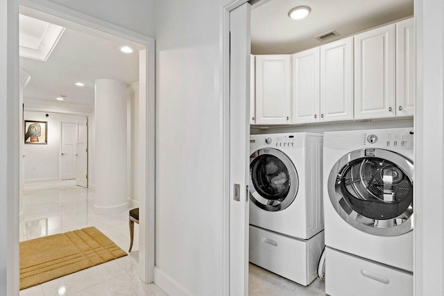 clothes washing area featuring light tile floors, washer and clothes dryer, and cabinets