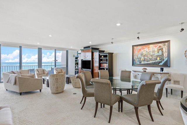 dining space with light colored carpet, a wall of windows, crown molding, and a water view