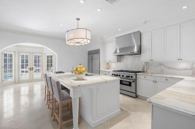 kitchen with a center island, wall chimney exhaust hood, premium appliances, tasteful backsplash, and pendant lighting