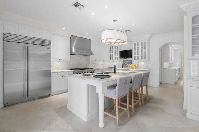 kitchen featuring backsplash, built in refrigerator, wall chimney range hood, and white cabinets