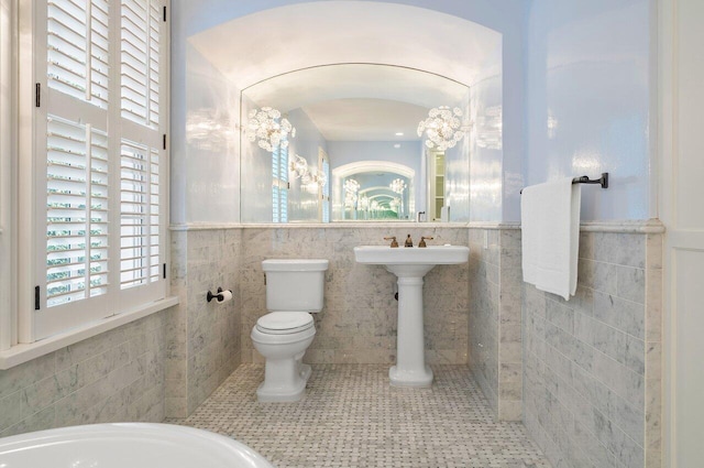 bathroom featuring toilet, tile floors, tile walls, and a bath