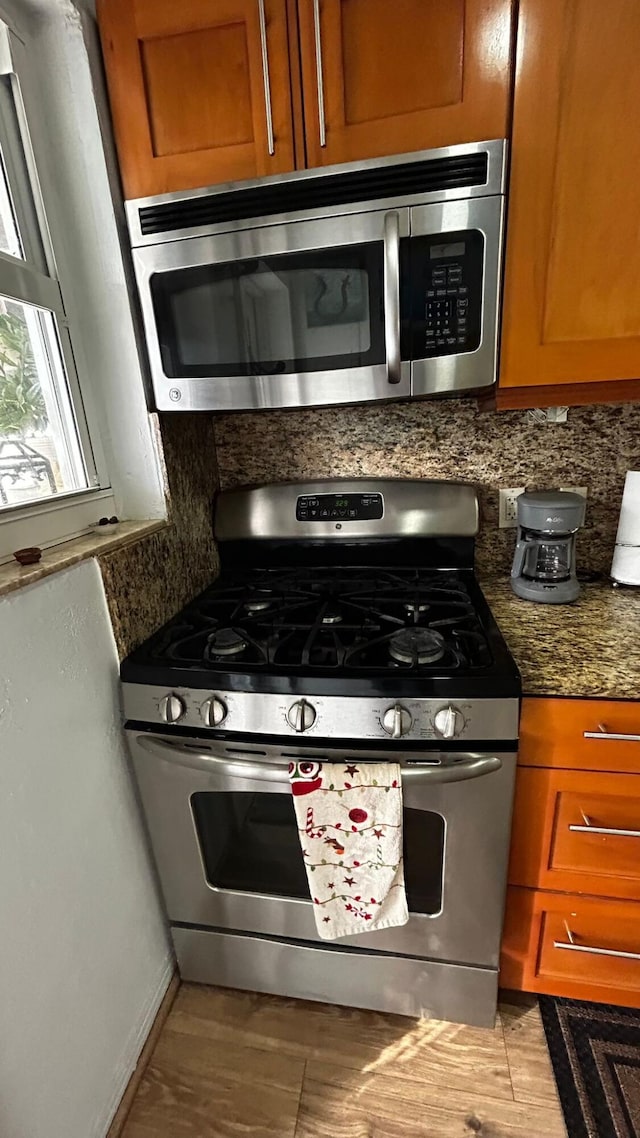 kitchen featuring stainless steel appliances, dark stone countertops, decorative backsplash, and light hardwood / wood-style floors