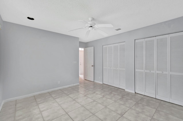 unfurnished bedroom featuring light tile flooring, two closets, ceiling fan, and a textured ceiling