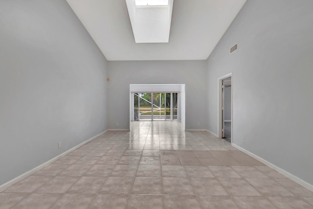 empty room featuring high vaulted ceiling, light tile flooring, and a skylight