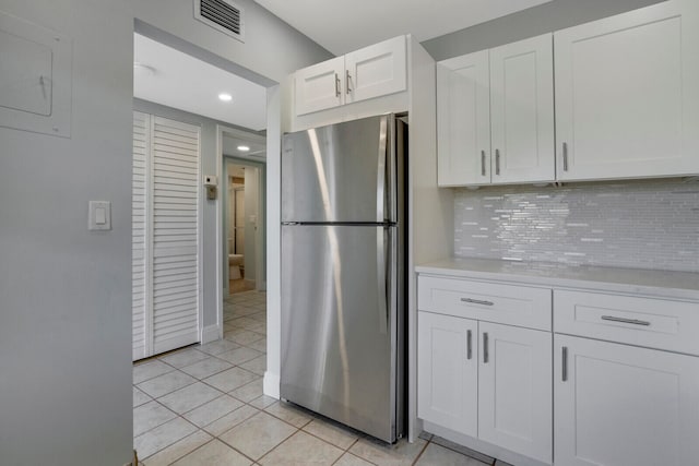 kitchen featuring stainless steel refrigerator, white cabinetry, backsplash, and light tile patterned flooring