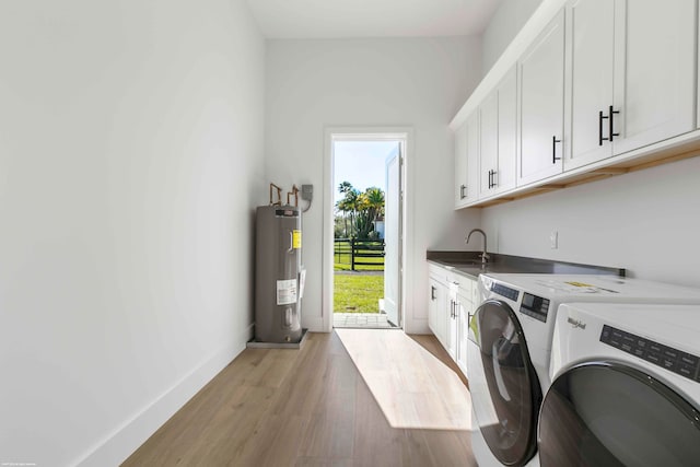 laundry area featuring electric water heater, sink, cabinets, washing machine and dryer, and light hardwood / wood-style floors