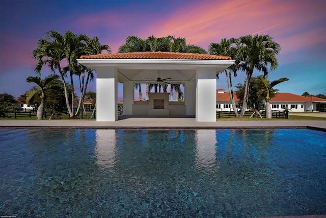 pool at dusk with a patio and ceiling fan