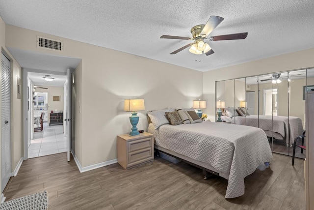 bedroom featuring ceiling fan, a textured ceiling, visible vents, and wood finished floors