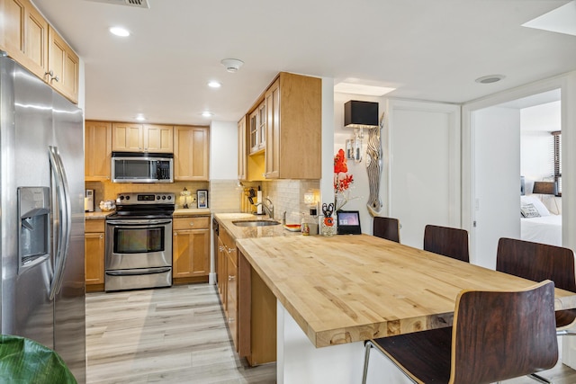 kitchen with wood counters, stainless steel appliances, tasteful backsplash, light wood-type flooring, and sink