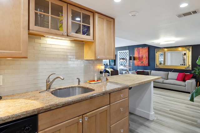 kitchen with light stone counters, backsplash, sink, and light hardwood / wood-style flooring