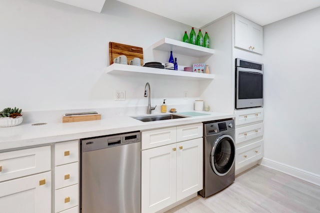 kitchen with washer / dryer, sink, white cabinetry, light wood-type flooring, and appliances with stainless steel finishes