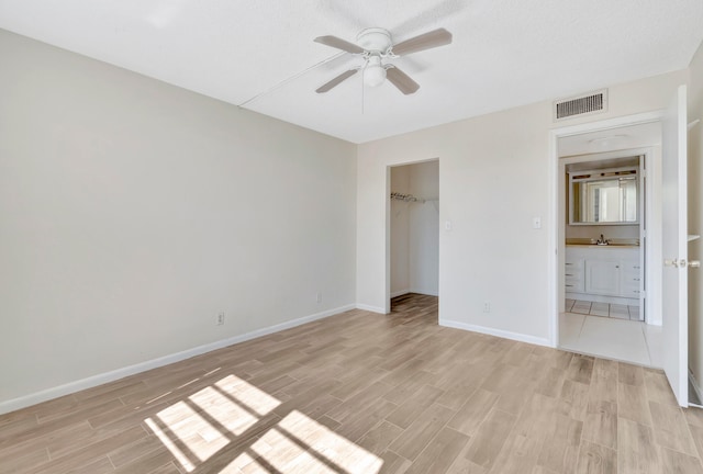 unfurnished bedroom with a spacious closet, a closet, sink, ceiling fan, and light wood-type flooring