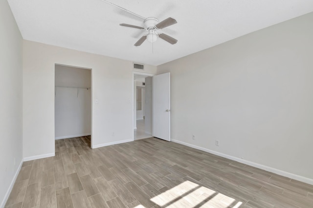 unfurnished bedroom featuring light wood-type flooring, a walk in closet, ceiling fan, and a closet