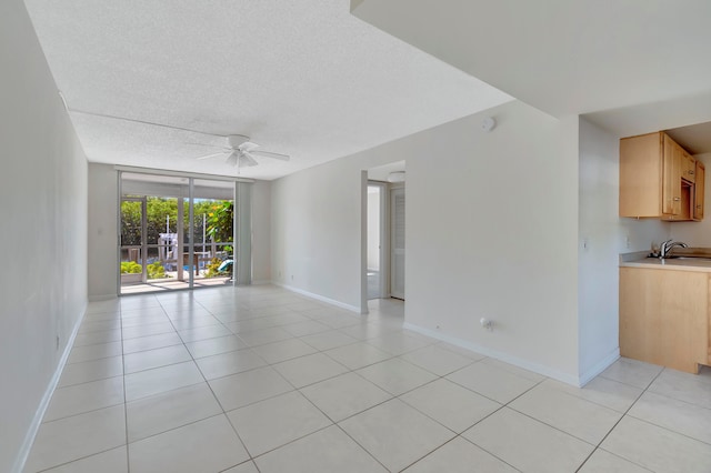 tiled empty room featuring a textured ceiling, floor to ceiling windows, ceiling fan, and sink