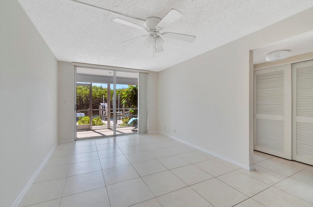 tiled spare room featuring a wall of windows, ceiling fan, and a textured ceiling