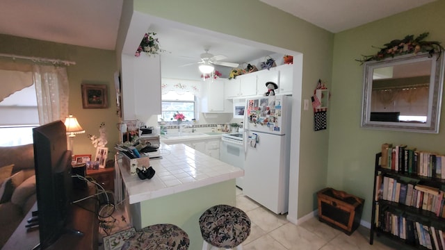 22 Northampton A, West Palm Beach, FL 33417 - kitchen featuring white appliances, tile counters, white cabinetry, a ceiling fan, and light tile patterned flooring