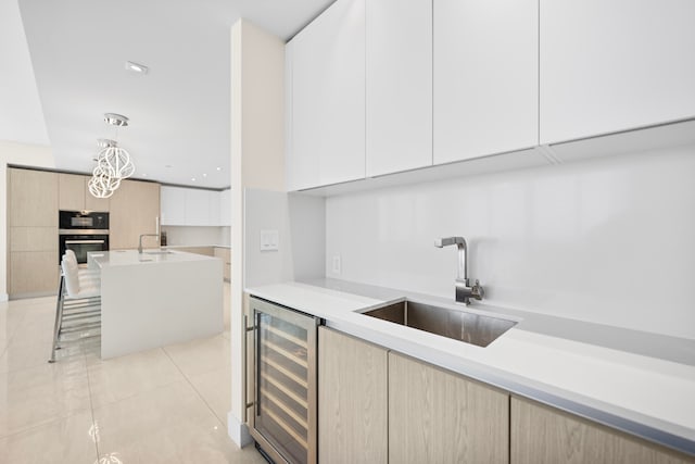 kitchen featuring light tile patterned flooring, decorative light fixtures, sink, white cabinets, and beverage cooler