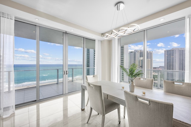 tiled dining space with a chandelier, expansive windows, a water view, and a view of the beach