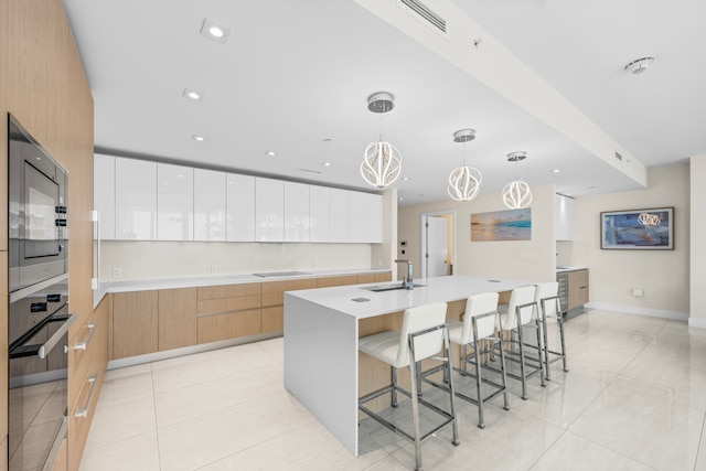 kitchen featuring sink, white cabinetry, appliances with stainless steel finishes, a large island with sink, and decorative light fixtures