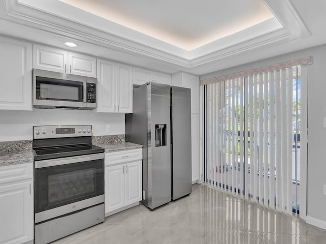 kitchen featuring white cabinetry, light stone countertops, appliances with stainless steel finishes, and a tray ceiling