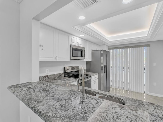 kitchen with white cabinets, appliances with stainless steel finishes, light stone countertops, and a raised ceiling