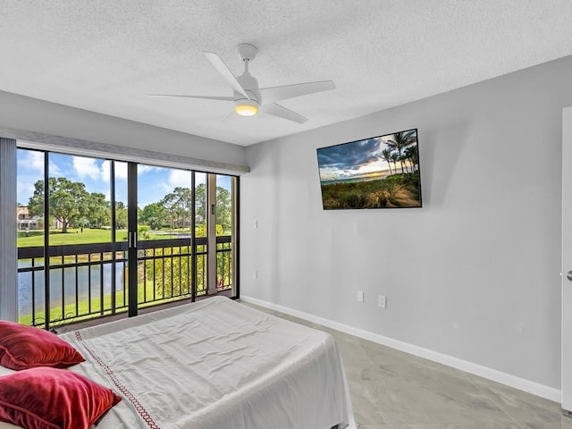 bedroom featuring a textured ceiling, concrete floors, access to exterior, ceiling fan, and a water view