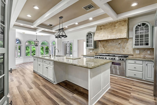 kitchen featuring custom exhaust hood, coffered ceiling, a center island with sink, and high end stove