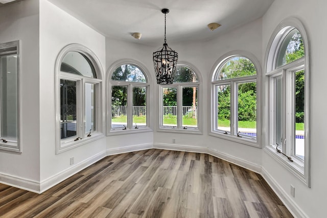 unfurnished dining area with wood-type flooring, a wealth of natural light, and a chandelier