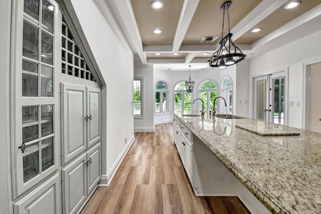 kitchen featuring sink, light stone countertops, light hardwood / wood-style floors, white cabinets, and decorative light fixtures