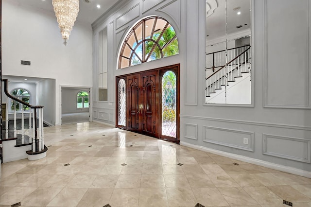 entrance foyer with crown molding, a towering ceiling, light tile patterned floors, and a notable chandelier