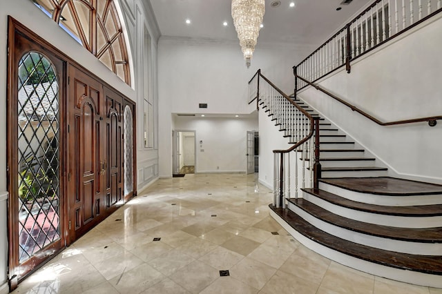 foyer with crown molding, a towering ceiling, and a notable chandelier