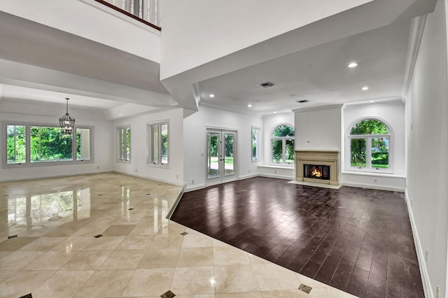 unfurnished living room with ornamental molding, light wood-type flooring, a chandelier, and french doors