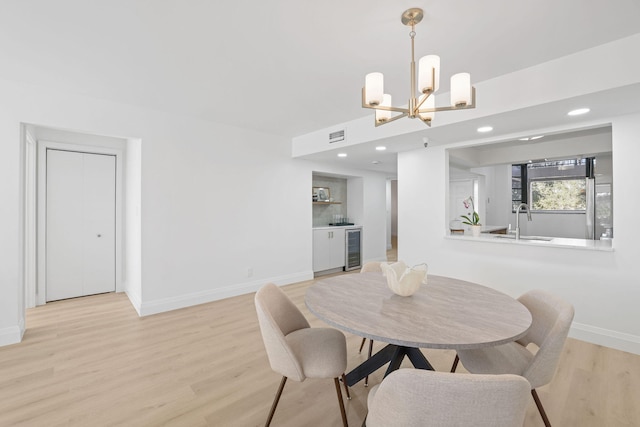 dining area with wine cooler, sink, a chandelier, and light wood-type flooring