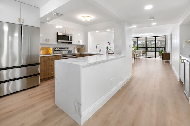 kitchen with light stone countertops, white cabinetry, light wood-type flooring, and stainless steel appliances