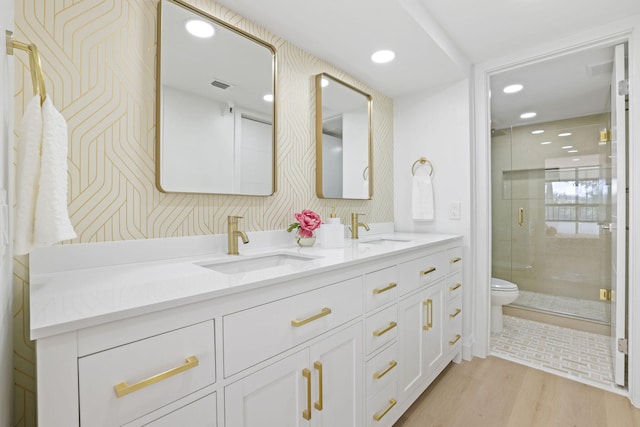 bathroom with toilet, dual bowl vanity, a shower with shower door, and wood-type flooring