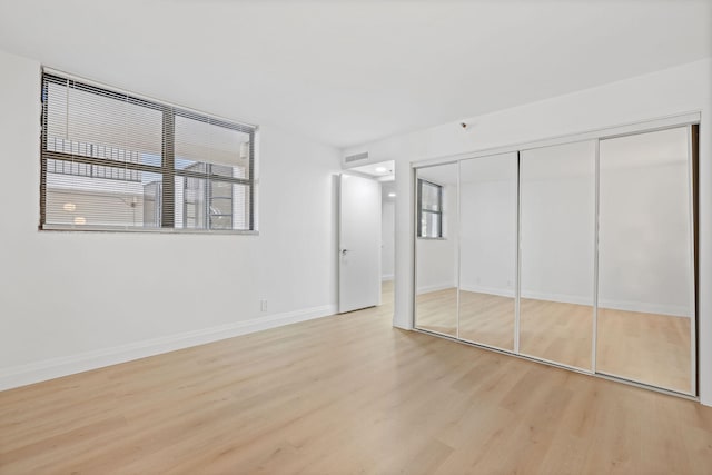 unfurnished bedroom featuring a closet, multiple windows, and light wood-type flooring