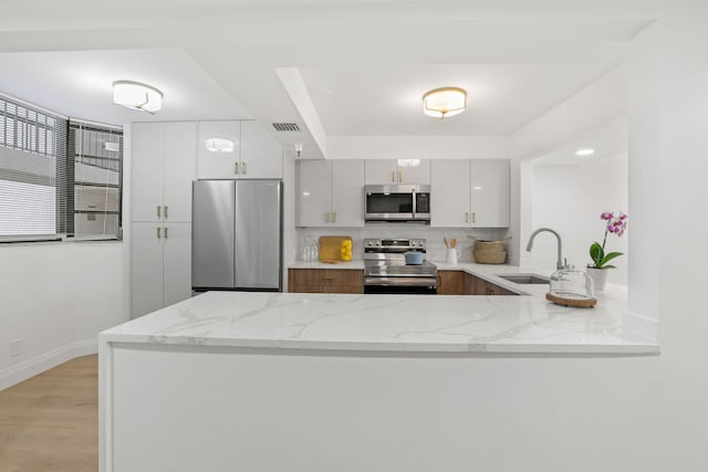 kitchen featuring white cabinets, appliances with stainless steel finishes, light stone countertops, and sink