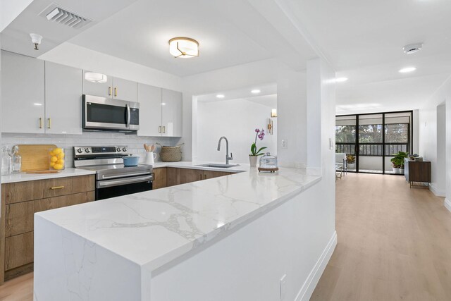 kitchen featuring light hardwood / wood-style floors, stainless steel appliances, white cabinetry, sink, and light stone counters